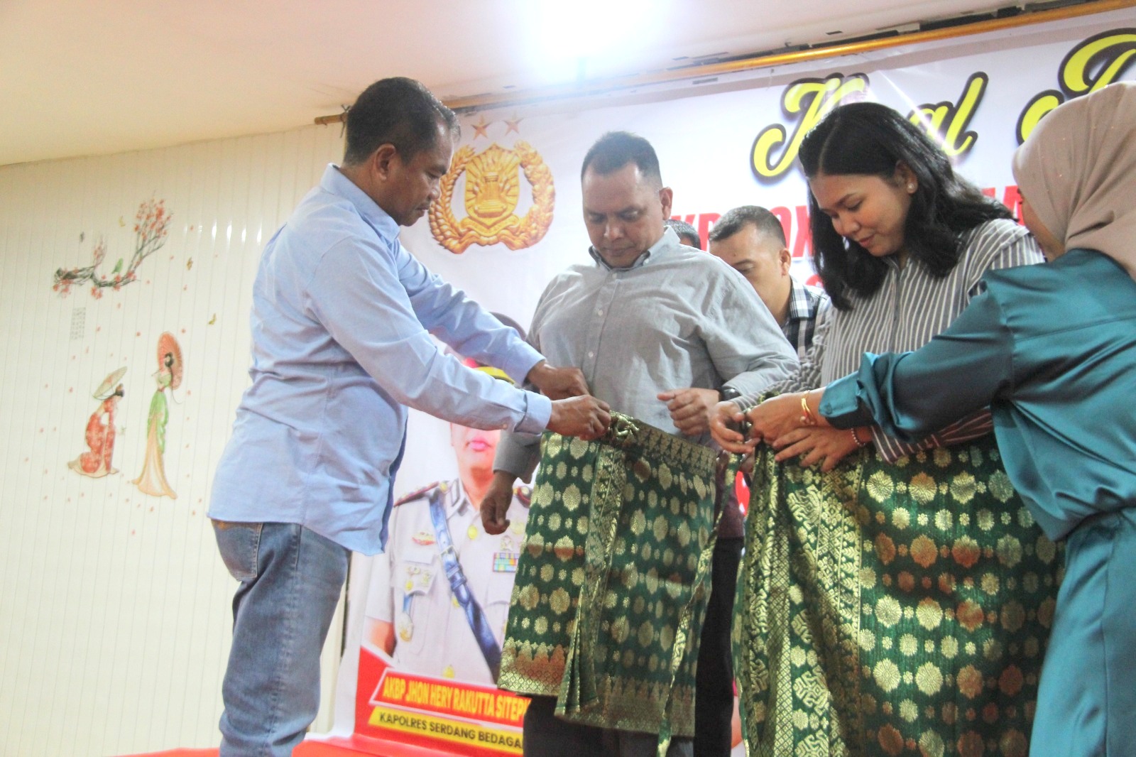 Teks Foto:Bupati Serdang Bedagai Darma Wijaya, memapaikan kain ke Kapolres Sergai yang baru AKBP Khon Hery Rakutta Sitepu, SIK, MH beserta ibu di aula titik temu Perbaungan, Sabtu, 6 Juli 2024.(Beritasore-Azwen)